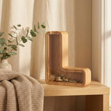 Personalised wooden letter money box in solid oak with clear coin window, styled on a nursery shelf